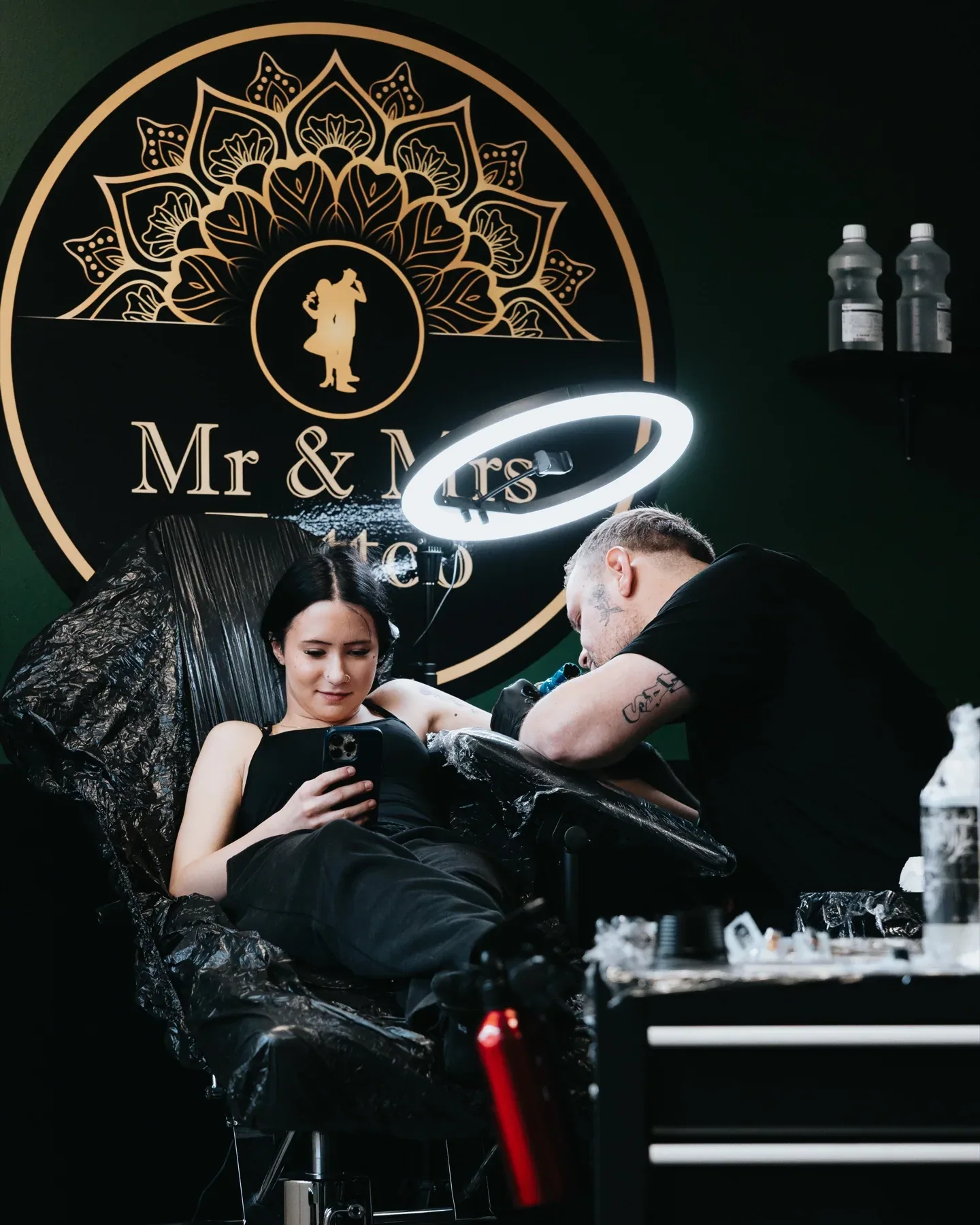 En artist tatoverer en kunde foran Mr & Mrs Tattoos logo på væggen